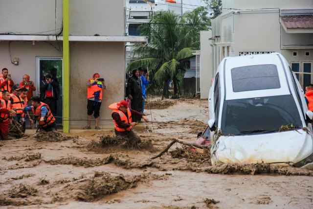 Rescuers wade through flood waters by holding a rope in their effort to evacuate residents who are trapped at their houses in Padang, West Sumatra province on November 27, 2025. (Photo by REZAN SOLEH / AFP)