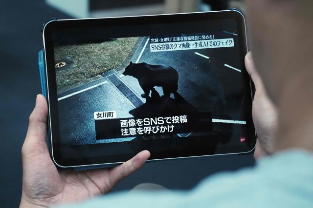 A man watches a local TV news report featuring a fake photo of a bear created using AI-generated that was posted on social media, in Tokyo on November 27, 2025. A Japanese town deleted a social media post warning of a bear sighting after discovering that a picture it had received showing the fearsome creature was AI-generated. (Photo by Kazuhiro NOGI / AFP)