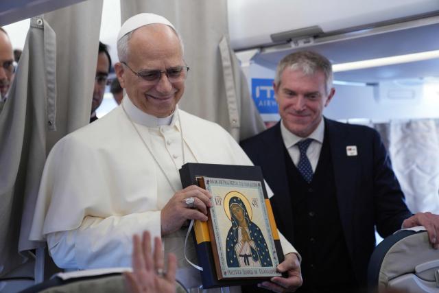 Pope Leo XIV holds an icon as he greets reporters aboard a flight on his way to Ankara on November 27, 2025. Pope Leo XIV arrived in Turkey on the first overseas trip of his papacy, which will also take him to Lebanon. (Photo by Domenico Stinellis / POOL / AFP)