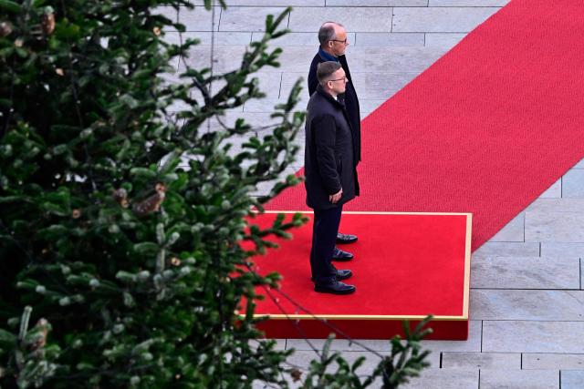 Germany's Chancellor Friedrich Merz (rear) and Estonia's Prime Minister Kristen Michal stand next to the Chancellery's Christmas tree as they listen to their national anthems during an official welcome ceremony in front of the Chancellery in Berlin, Germany, on November 27, 2025. (Photo by John MACDOUGALL / POOL / AFP)