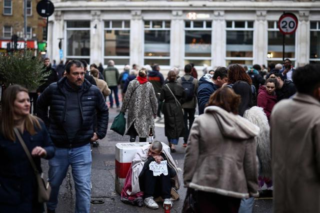 A man (C) sits with a sign asking for money, as people walk near Borough Market, one of the city's oldest food markets, just south of the River Thames in London on November 27, 2025. (Photo by Henry NICHOLLS / AFP)
