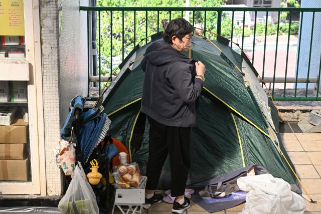 A displaced resident stands outside her tent inside a shopping mall near the scene of a major fire that swept through several apartment blocks at the Wang Fuk Court residential estate in Hong Kong's Tai Po district on November 28, 2025. Firefighters searched the last of the housing estate flats torched by Hong Kong's worst fire in decades on November 28, with the death toll rising to at least 94 overnight and scores still missing. (Photo by Peter PARKS / AFP)
