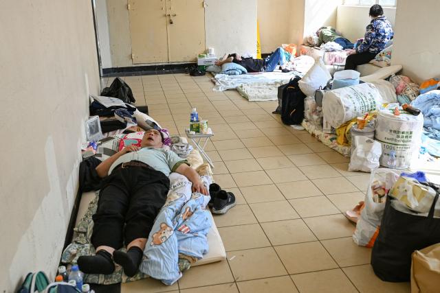 Displaced residents are seen at a makeshift shelter inside a shopping mall near the scene of a major fire that swept through several apartment blocks at the Wang Fuk Court residential estate in Hong Kong's Tai Po district on November 28, 2025. Firefighters searched the last of the housing estate flats torched by Hong Kong's worst fire in decades on November 28, with the death toll rising to at least 94 overnight and scores still missing. (Photo by Peter PARKS / AFP)