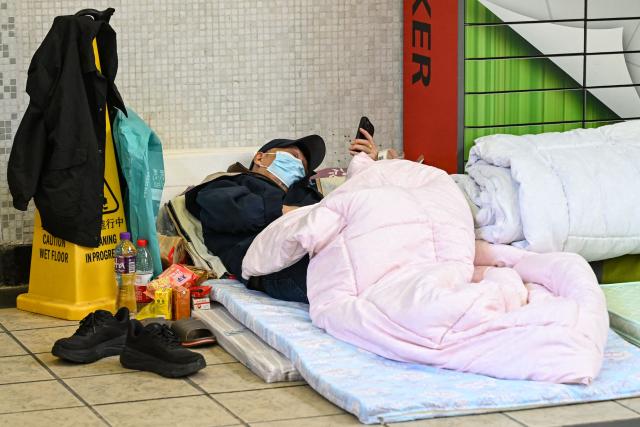 A displaced resident is seen at a makeshift shelter inside a shopping mall near the scene of a major fire that swept through several apartment blocks at the Wang Fuk Court residential estate in Hong Kong's Tai Po district on November 28, 2025. Firefighters searched the last of the housing estate flats torched by Hong Kong's worst fire in decades on November 28, with the death toll rising to at least 94 overnight and scores still missing. (Photo by Peter PARKS / AFP)