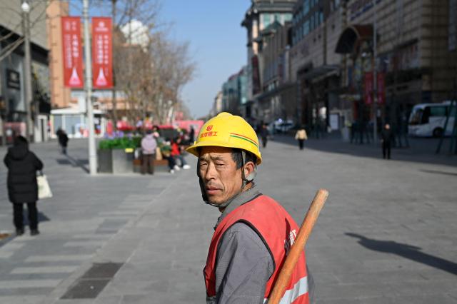 A worker looks back as he walks along a shopping street in Beijing on November 28, 2025. (Photo by WANG Zhao / AFP)