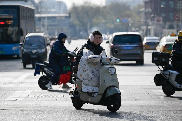 People ride electric scooters along a shopping street in Beijing on November 28, 2025. (Photo by WANG Zhao / AFP)
