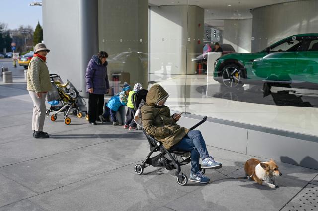 People rest outside an electric car showroom in Beijing on November 28, 2025. (Photo by WANG Zhao / AFP)
