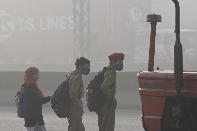 Children wearing masks walk to school, amid dense smog in Lahore on November 28, 2025. (Photo by Arif ALI / AFP)