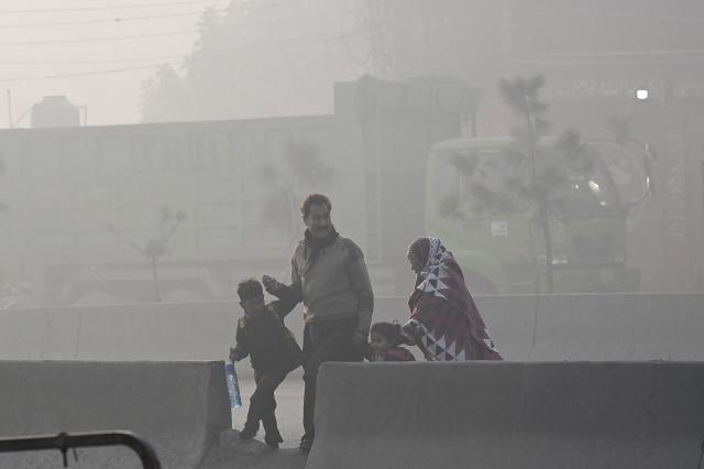 People cross a road amid dense smog in Lahore on November 28, 2025. (Photo by Arif ALI / AFP)