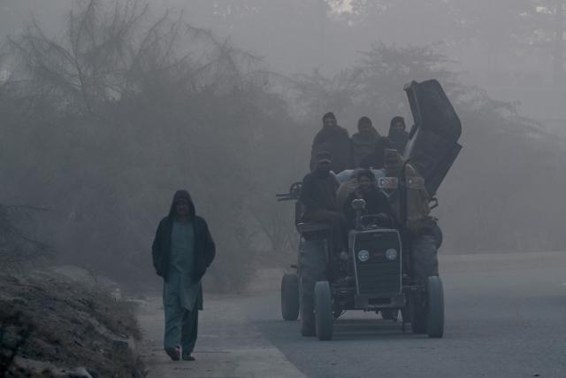 Commuters ride a tractor along a road, amid dense smog in Lahore on November 28, 2025. (Photo by Arif ALI / AFP)
