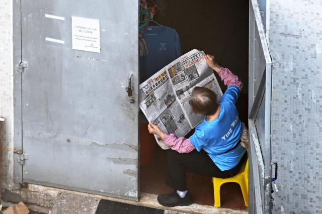A woman reads a newspaper about the major fire that swept through several apartment blocks at the Wang Fuk Court residential estate in Hong Kong's Tai Po district on November 28, 2025. Families of the scores still missing after Hong Kong's worst blaze in decades scoured hospitals Friday as firefighting operations ended, with the death toll at least 94. (Photo by Peter PARKS / AFP)