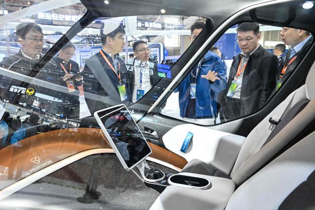 People stand next to a VoloCity eVolt aircraft seen in the Volocopter booth during the Aero Asia 2025 in Zhuhai, in southern China's Guangdong province on November 28, 2025. Aero Asia 2025 is an international aviation and aerospace exhibition that runs between November 27 and 30. (Photo by Hector RETAMAL / AFP)