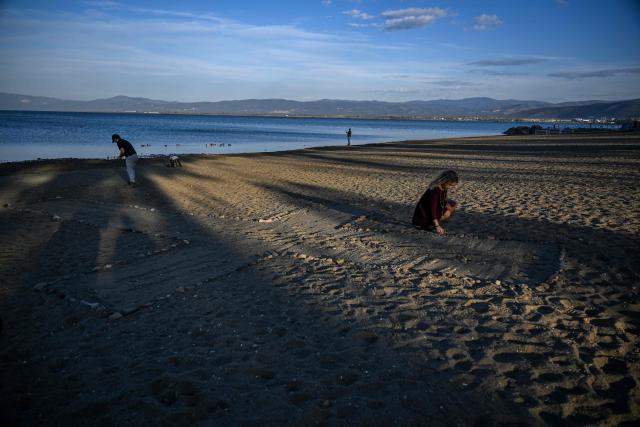 Spanish tourist Irati Aguirre 26 (R) and New Zelander Thomas Libeau 32, draw a cross with stones on the beach as they wait for the arrival of Pope Leo XIV next to remains of the sunken Byzantine Basilica of the Holy Fathers on the shore of Lake Iznik, in Iznik, on November 28, 2025. Pope Leo XIV is on a four-day visit to Turkey. (Photo by Ozan KOSE / AFP)