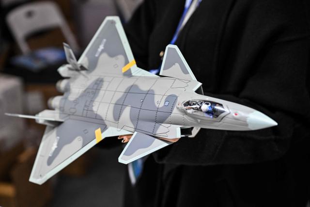 A woman holds a scale model replica of the Chinese-made Chengdu J-20 stealth fighter in a booth during the Aero Asia 2025 in Zhuhai, in southern China's Guangdong province on November 28, 2025. Aero Asia 2025 is an international aviation and aerospace exhibition that runs between November 27 and 30. (Photo by Hector RETAMAL / AFP)