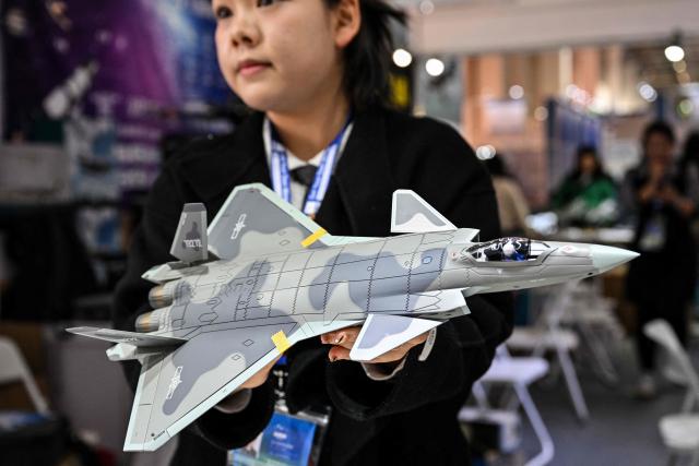 A woman holds a scale model replica of the Chinese-made Chengdu J-20 stealth fighter in a booth during the Aero Asia 2025 in Zhuhai, in southern China's Guangdong province on November 28, 2025. Aero Asia 2025 is an international aviation and aerospace exhibition that runs between November 27 and 30. (Photo by Hector RETAMAL / AFP)