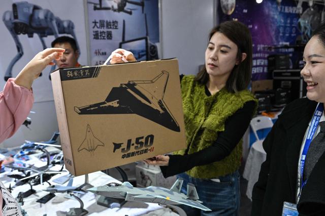 A woman sells a scale model replica of the Chinese-made J-50 fighter in a booth during the Aero Asia 2025 in Zhuhai, in southern China's Guangdong province on November 28, 2025. Aero Asia 2025 is an international aviation and aerospace exhibition that runs between November 27 and 30. (Photo by Hector RETAMAL / AFP)