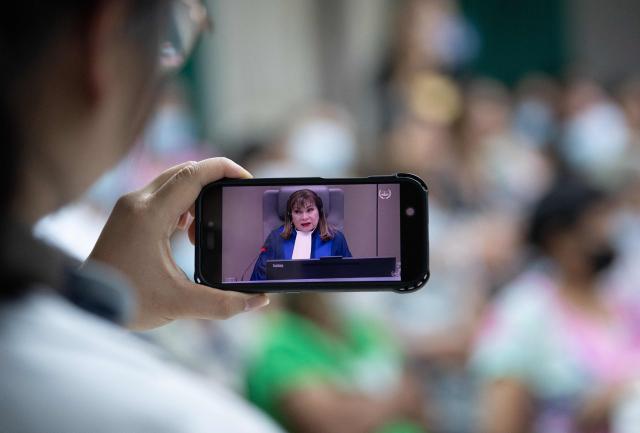 A woman watches an International Criminal Court (ICC) judge on her phone next to relatives (R) of victims of extrajudicial killings during the live streaming of the hearing on the appeal ruling on the provisional release of former Philippine president Rodrigo Duterte, who is accused of crimes against humanity, at a religious house in Manila on November 28, 2025. (Photo by Ted ALJIBE / AFP)
