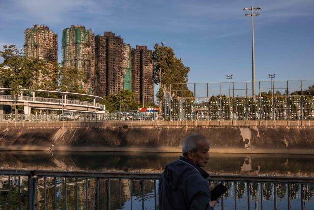EDITORS NOTE: Graphic content / A man stands before the aftermath of a major fire that swept through several apartment blocks at the Wang Fuk Court residential estate in Hong Kong's Tai Po district on November 28, 2025. The death toll from Hong Kong's worst blaze in decades rose to 128 on November 28, with dozens still missing, as authorities said fire alarms in the residential estate buildings had been malfunctioning. (Photo by Dale DE LA REY / AFP)