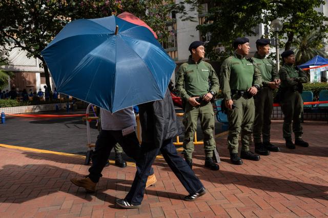 EDITORS NOTE: Graphic content / A woman (front C) is shielded by an umbrella as she visited a community centre to look at photographs of victims for identification in the aftermath of a major fire that swept through several apartment blocks at the Wang Fuk Court residential estate in Hong Kong's Tai Po district on November 28, 2025. The death toll from Hong Kong's worst blaze in decades rose to 128 on November 28, with dozens still missing, as authorities said fire alarms in the residential estate buildings had been malfunctioning. (Photo by Dale DE LA REY / AFP)