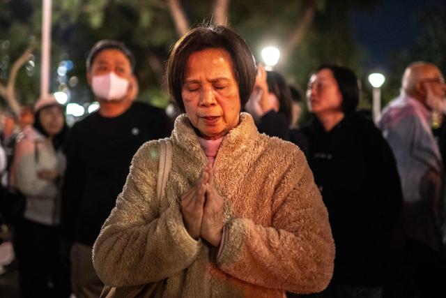 A woman prays at the aftermath of a major fire that swept through several apartment blocks at the Wang Fuk Court residential estate in Hong Kong's Tai Po district on November 28, 2025. The death toll from Hong Kong's worst blaze in decades rose to 128 on november 28, with dozens still missing, as authorities said fire alarms in the residential estate buildings had been malfunctioning. (Photo by Philip FONG / AFP)