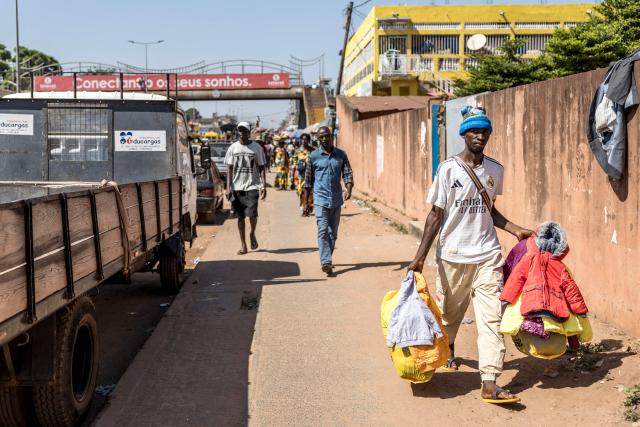 TOPSHOT - A vendor carries clothes at a market in Bissau, on November 28, 2025. Life limped back to normal on Friday in the capital of volatile Guinea-Bissau after the west African nation's fifth coup that came on the heels of presidential and parliamentary polls.
The military appointed General Horta N'Tam, the army's chief of staff, as the country's new leader for a transition period of one year after Wednesday's putsch. The takeover came just one day before authorities had been due to announce the provisional results of the November 23 polls. There were vehicles and taxis along the main road from the port of the seaside capital Bissau to the presidential palace, as well as pedestrians (Photo by PATRICK MEINHARDT / AFP)