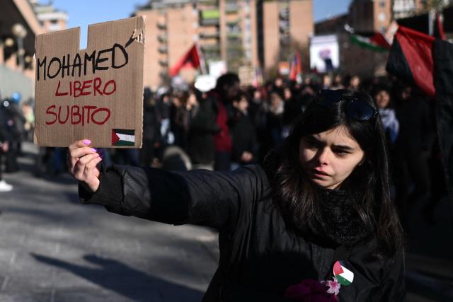 A woman holds a placard “Free Mohamed Shahin” one of the Iman of Turin detained in Italy, during a nationwide strike organized by the Unione Sindacale di Base (USB Union) in Turin, northwestern Italy on November 28, 2025. Trade unions have called a strike for public and private sector workers, affecting transport, schools, healthcare, and other public services. The reasons behind the strike are linked to the 2026 Economic Plan, which is being contested by the union groups CUB, USB, SGB, COBAS, and USI-CIT, who oppose the increase in military spending at the expense of essential public services. (Photo by MARCO BERTORELLO / AFP)