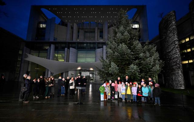 German Chancellor Friedrich Merz (R, behind his young guests) stands next to children as they pose for a picture during an official event to hand over the Christmas tree for the Chancellery, on November 28, 2025 in front of the Chancellery in Berlin. (Photo by Tobias SCHWARZ / AFP)