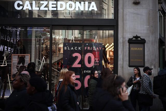 Shoppers pass window displays advertising Black Friday discounted sales in central London on November 28, 2025. (Photo by HENRY NICHOLLS / AFP)