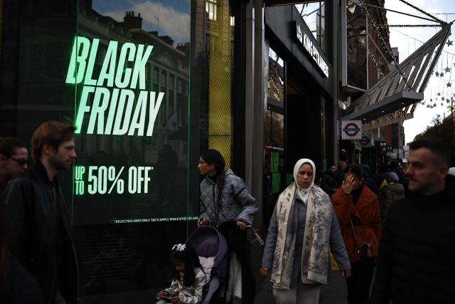 Shoppers pass window displays advertising Black Friday discounted sales in central London on November 28, 2025. (Photo by HENRY NICHOLLS / AFP)