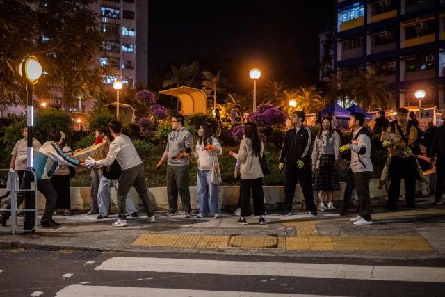Volunteers form a human chain to move the boxes of goods away from the area near the aftermath of 7a major fire that swept through several apartment blocks at the Wang Fuk Court residential estate in Hong Kong's Tai Po district on November 28, 2025. The raging fire at Wang Fuk Court claimed at least 128 lives in what was the world's deadliest residential building fire since 1980, and authorities said Friday the status of around 200 people remained "unclear". (Photo by Philip FONG / AFP)