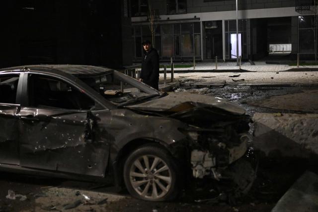 A local resident looks at a damaged car in the courtyard of a damaged residential building following a drone attack in Kyiv on November 29, 2025, amid the Russian invasion in Ukraine. A Russian drone attack targeted the Ukrainian capital in the early hours of November 29, 2025, wounding seven people, authorities in Kyiv said. (Photo by Sergei GAPON / AFP)