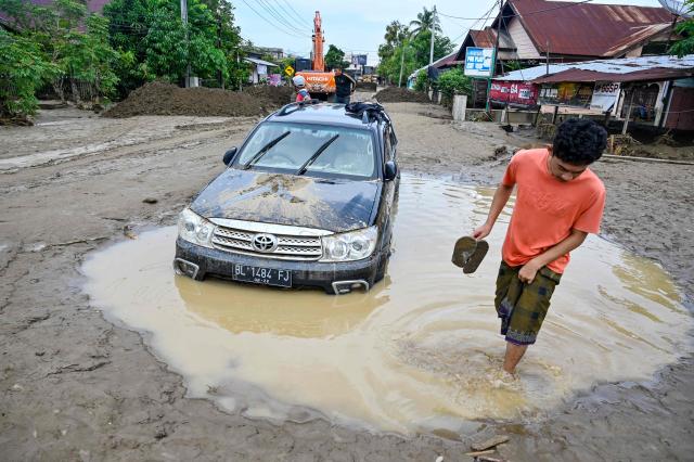 A resident walks past a stranded car stuck in deep mud following flash floods in Meureudu, Pidie Jaya district in Indonesia's Aceh province on November 28, 2025. Days of devastating flooding across Southeast Asia have killed more than 300 people in Indonesia, Thailand and Malaysia, authorities said on November 28. (Photo by CHAIDEER MAHYUDDIN / AFP)