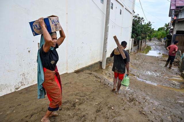 A resident carries food supplies following flash floods in Meureudu, Pidie Jaya district in Indonesia's Aceh province on November 28, 2025. Days of devastating flooding across Southeast Asia have killed more than 300 people in Indonesia, Thailand and Malaysia, authorities said on November 28. (Photo by CHAIDEER MAHYUDDIN / AFP)