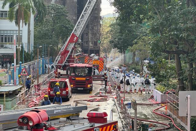 Police officers from the Disaster Victim Identification Unit (DVIU), dressed in white-coloured full-body protective gear, enter one of the housing blocks of Wang Fuk Court in Hong Kong on November 29, 2025. Hong Kong's leader and top government officials observed a moment of silence on November 29 to mourn the victims of the city's deadliest fire in decades, which killed at least 128 people and displaced hundreds. (Photo by Yan ZHAO / AFP)