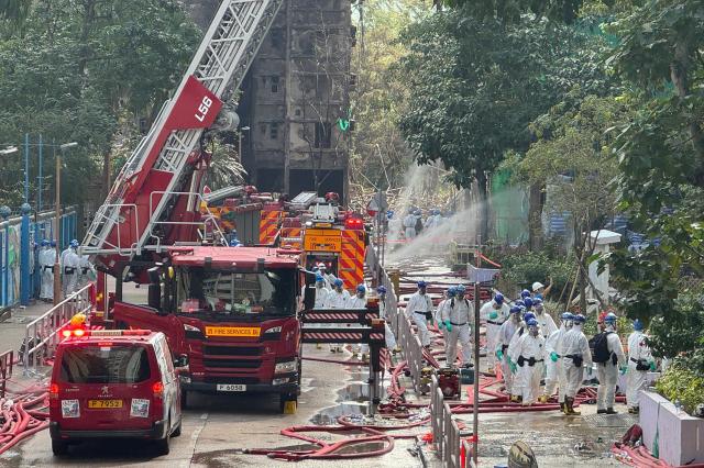 Police officers from the Disaster Victim Identification Unit (DVIU), dressed in white-coloured full-body protective gear, enter one of the housing blocks of Wang Fuk Court in Hong Kong on November 29, 2025. Hong Kong's leader and top government officials observed a moment of silence on November 29 to mourn the victims of the city's deadliest fire in decades, which killed at least 128 people and displaced hundreds. (Photo by Yan ZHAO / AFP)