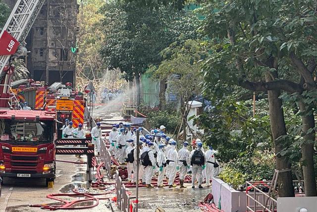 Police officers from the Disaster Victim Identification Unit (DVIU), dressed in white-coloured full-body protective gear, enter one of the housing blocks of Wang Fuk Court in Hong Kong on November 29, 2025. Hong Kong's leader and top government officials observed a moment of silence on November 29 to mourn the victims of the city's deadliest fire in decades, which killed at least 128 people and displaced hundreds. (Photo by Yan ZHAO / AFP)