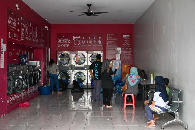 People queue to use coin-operated dryers at a laundromat in Karak, Malaysia’s Pahang state on November 29, 2025, as severe flooding affected thousands of people in the region following days of heavy rain. Flooding in Malaysia from days of heavy rain has swept through eight states, with forecasters predicting more rain in the coming days. Devastating flooding across Southeast Asia have killed more than 300 people in Indonesia, Thailand and Malaysia, authorities said on November 28. (Photo by Mohd RASFAN / AFP)