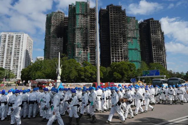 Police officers from the Disaster Victim Identification Unit (DVIU), dressed in white-coloured full-body protective gear, gather by the housing blocks of Wang Fuk Court in the aftermath of the deadly November 26 fire, in Hong Kong on November 29, 2025.  (Photo by Yan ZHAO / AFP)