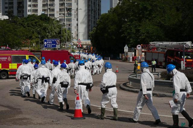 Police officers from the Disaster Victim Identification Unit (DVIU), dressed in white-coloured full-body protective gear, walk past the housing blocks of Wang Fuk Court in the aftermath of the deadly November 26 fire, in Hong Kong on November 29, 2025.  (Photo by Yan ZHAO / AFP)