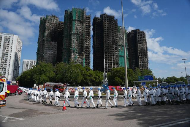 TOPSHOT - Police officers from the Disaster Victim Identification Unit (DVIU), dressed in white-coloured full-body protective gear, walk past the housing blocks of Wang Fuk Court in the aftermath of the deadly November 26 fire, in Hong Kong on November 29, 2025.  (Photo by Yan ZHAO / AFP)