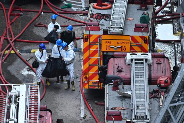 Police officers from the Disaster Victim Identification Unit (DVIU), dressed in white-coloured full-body protective gear, carry black bags outside the Wang Fuk Court in the aftermath of the deadly November 26 fire in Hong Kong's Tai Po district on November 29, 2025.  (Photo by Philip FONG / AFP)