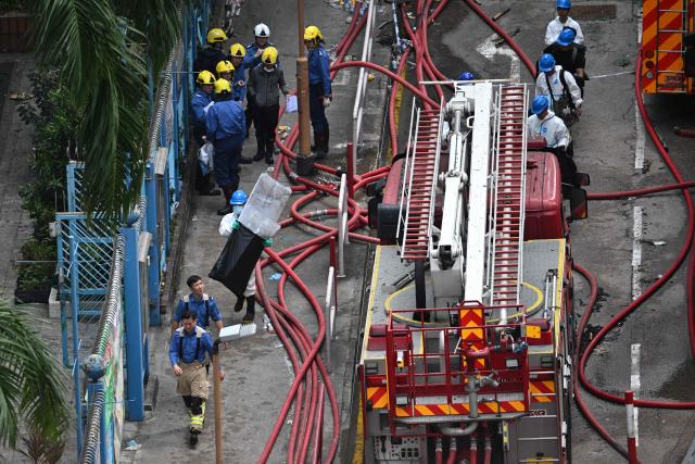 Emergency personnel (L in blue) and police officers from the Disaster Victim Identification Unit (DVIU), dressed in white-coloured full-body protective gear, work outside the Wang Fuk Court in the aftermath of the deadly November 26 fire in Hong Kong's Tai Po district on November 29, 2025.  (Photo by Philip FONG / AFP)