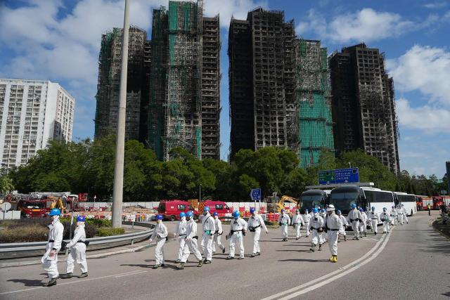 Police officers from the Disaster Victim Identification Unit (DVIU), dressed in white-coloured full-body protective gear, walk past the housing blocks of Wang Fuk Court in the aftermath of the deadly November 26 fire, in Hong Kong on November 29, 2025.  (Photo by Yan ZHAO / AFP)