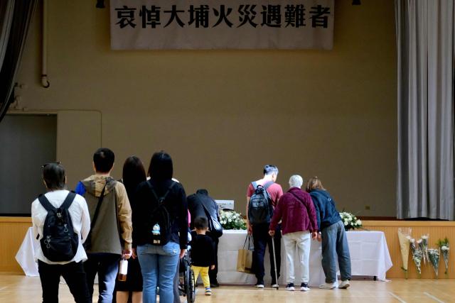 A banner (top) that reads "condolences to the victims of the Tai Po fire" is seen as mourners wait in line to pay their respects at a memorial point in Tai Po district, some two kilometres away from Wang Fuk Court housing estate, in the aftermath of the deadly November 26 fire in Hong Kong on November 29, 2025.  (Photo by Tommy WANG / AFP)