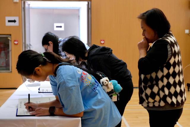 Mourners write in books as they pay their respects at a memorial point in Tai Po district, some two kilometres away from Wang Fuk Court housing estate, in the aftermath of the deadly November 26 fire in Hong Kong on November 29, 2025.  (Photo by Tommy WANG / AFP)