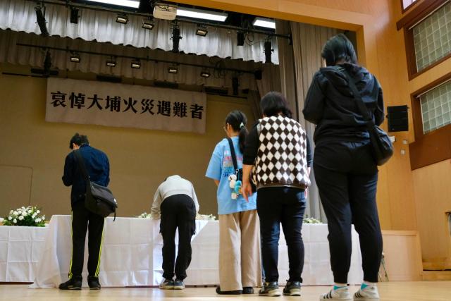 A banner (top) that reads "condolences to the victims of the Tai Po fire" is seen as mourners wait in line to pay their respects at a memorial point in Tai Po district, some two kilometres away from Wang Fuk Court housing estate, in the aftermath of the deadly November 26 fire in Hong Kong on November 29, 2025.  (Photo by Tommy WANG / AFP)