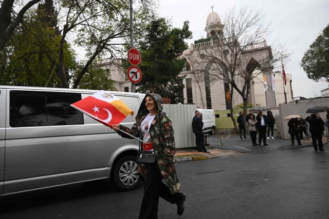 A woman walks with a Turkish/Vatican flag as Pope Leo XIV attends a private meeting with religious leaders at the Mor Ephrem Syriac Orthodox Church (background), in Istanbul on November 29, 2025. (Photo by YASIN AKGUL / AFP)