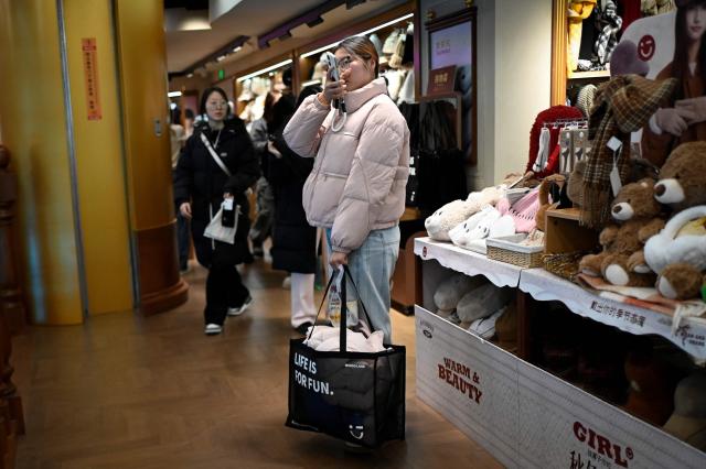 A woman carrying a shopping bag reacts as she visits a store in Beijing on November 29, 2025. (Photo by WANG Zhao / AFP)