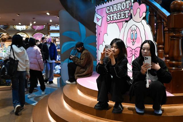Two women use their mobile phone at a store in Beijing on November 29, 2025. (Photo by WANG Zhao / AFP)
