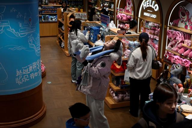 A woman reacts as she tries on a hat at a store in Beijing on November 29, 2025. (Photo by WANG Zhao / AFP)